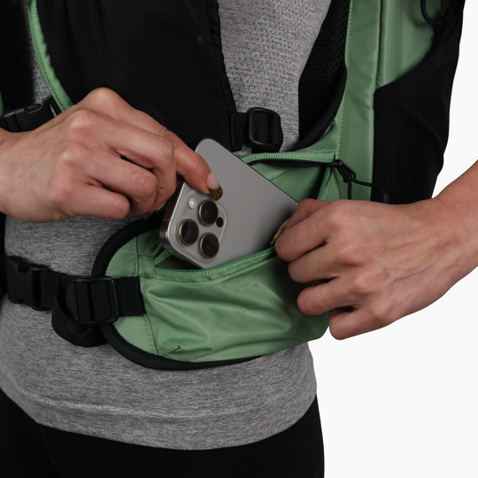 Phone being placed inside the zippered hip belt pocket of the sage green Canyon Elite 25 pack